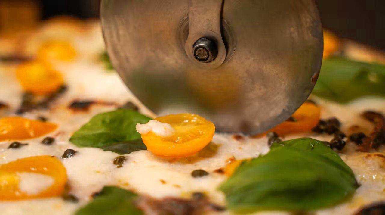 Rotella che taglia una pizza con datterini gialli e basilico