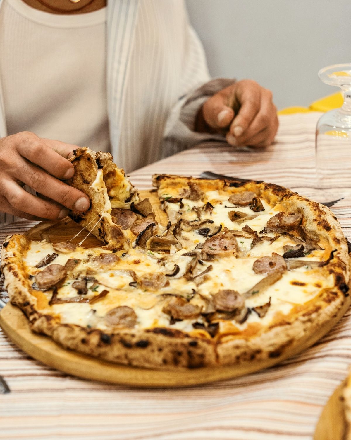 Pizza con salsiccia e funghi, una fetta sollevata con il formaggio filante